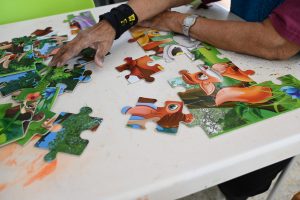 ידיים מרכיבות פאזל צבעוני עם דמויות מצוירות של חיות על שולחן לבן.